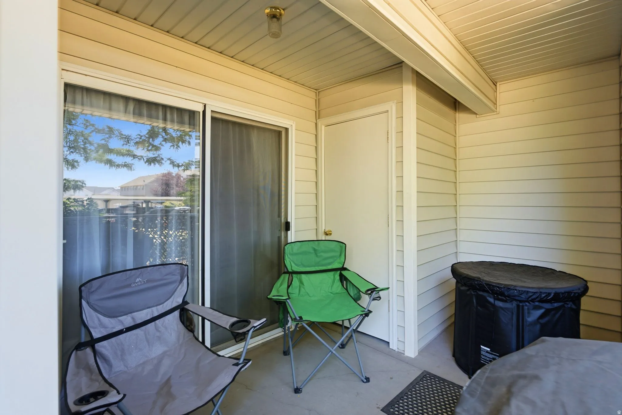 Covered outdoor patio featuring beige siding, concrete flooring, and an exterior storage door