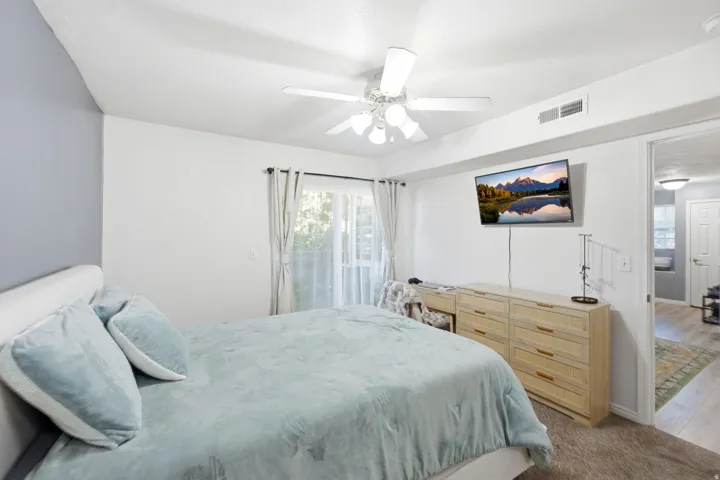 Master bedroom featuring a ceiling fan, light-toned carpeting, and a sliding glass door with sheer and blackout curtains