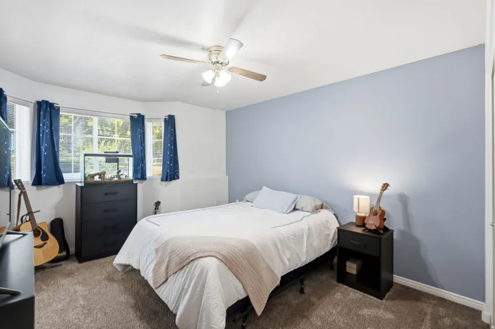 Carpeted room featuring a ceiling fan with integrated lighting, a bay window with multiple panes, a contrasting accent wall, and white baseboards