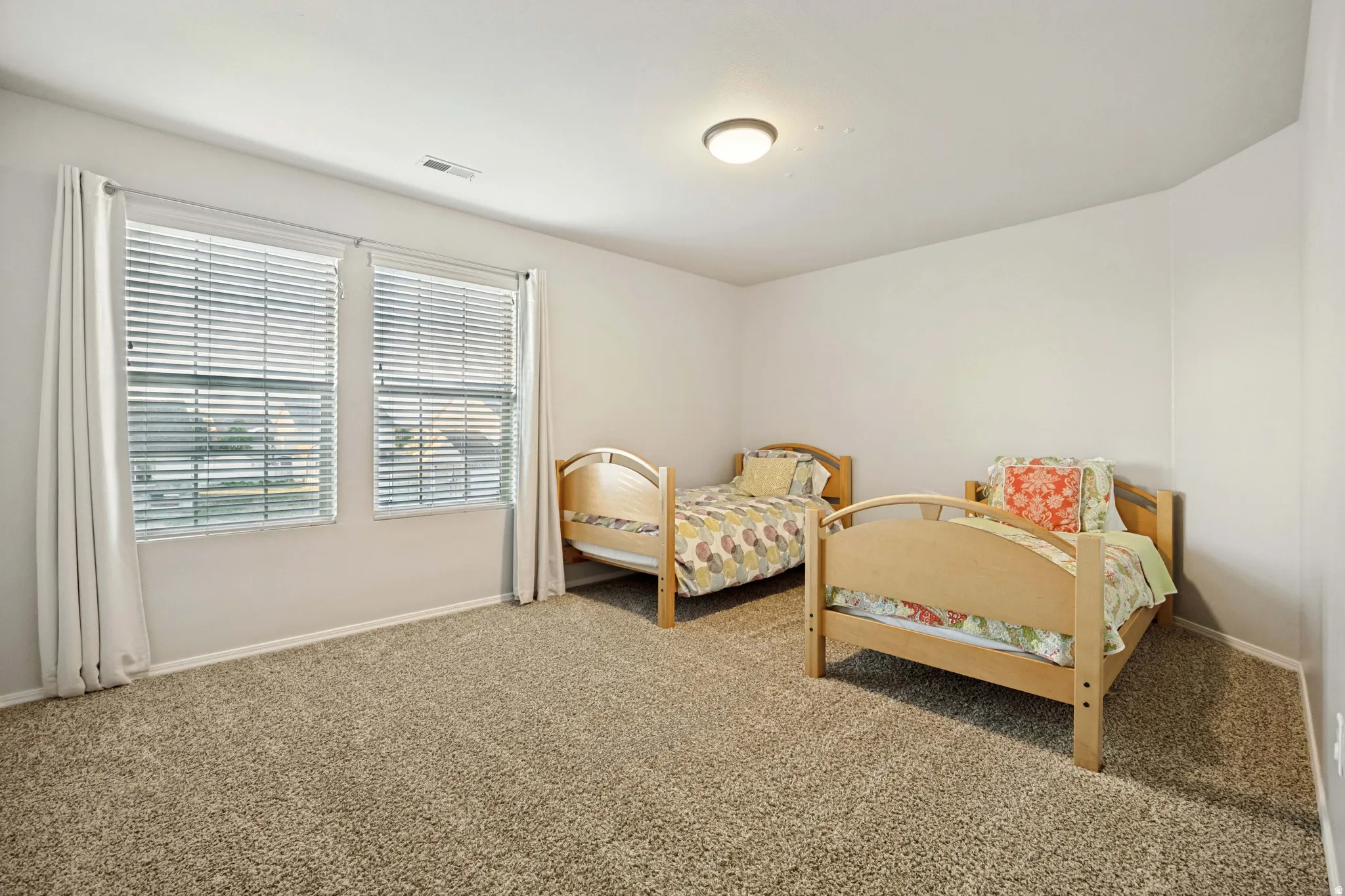 Room featuring neutral wall tones, two windows with blinds, a ceiling-mounted light fixture, and carpeted flooring