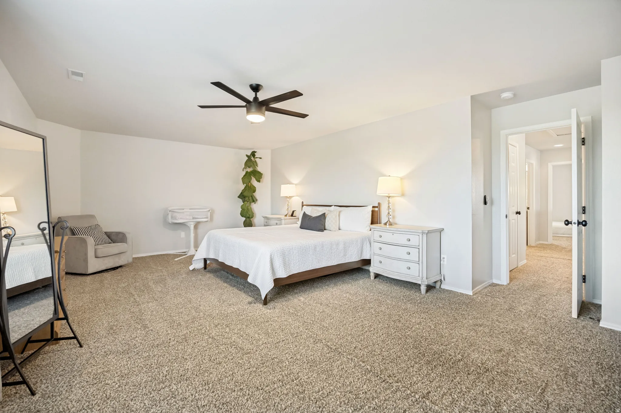 Spacious bedroom featuring neutral wall tones, plush carpeting, a modern ceiling fan, and ample natural light