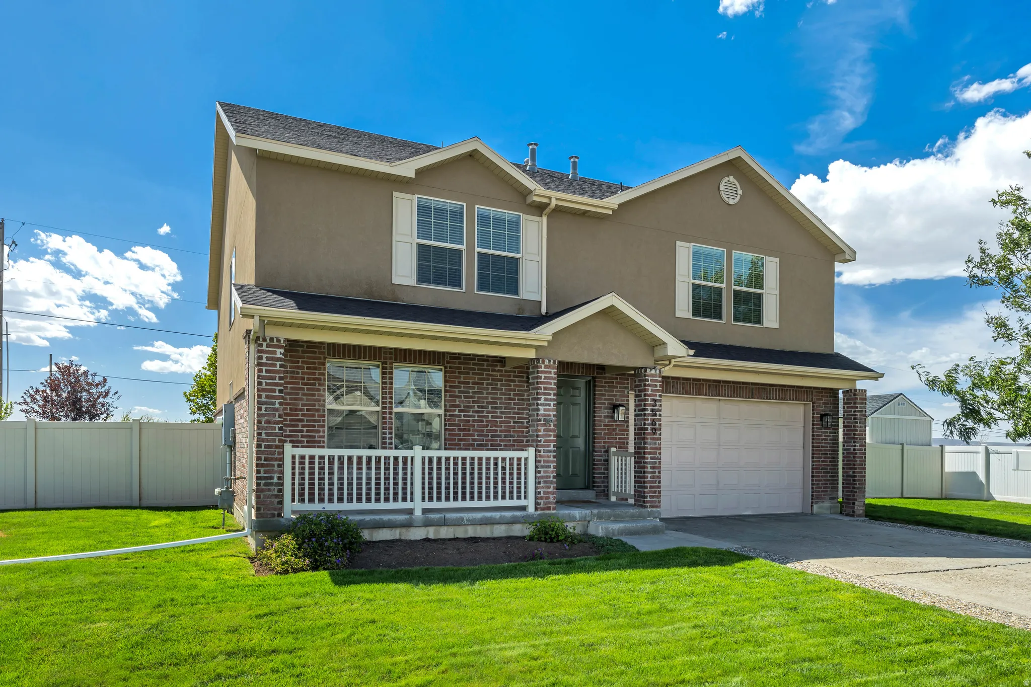Two-story residence featuring a brick facade, stucco siding, an attached garage, a covered front porch with white railing, and a vibrant green lawn