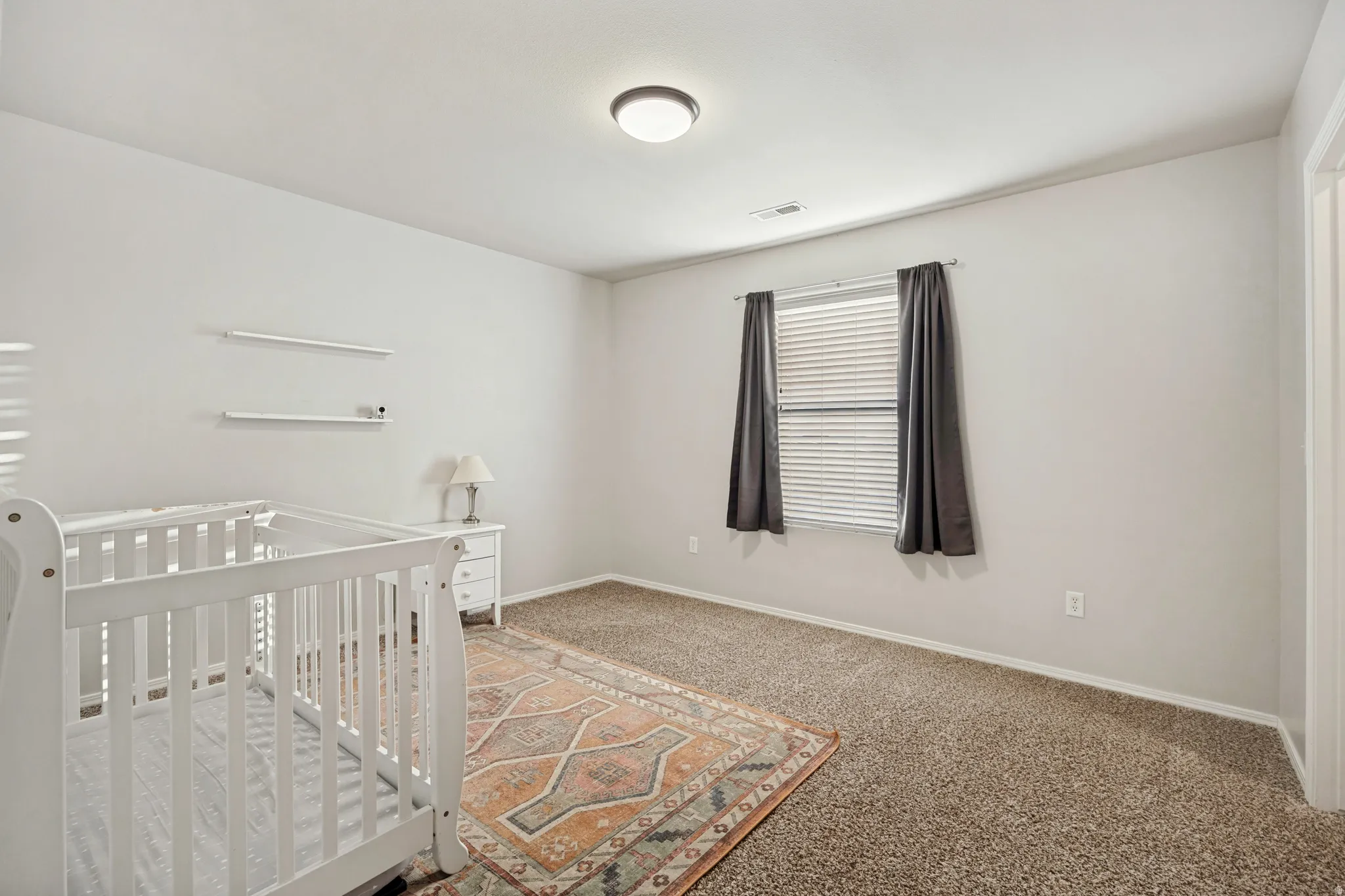 Neutral wall paint with carpeted flooring, featuring a window with blinds and dark-toned curtains