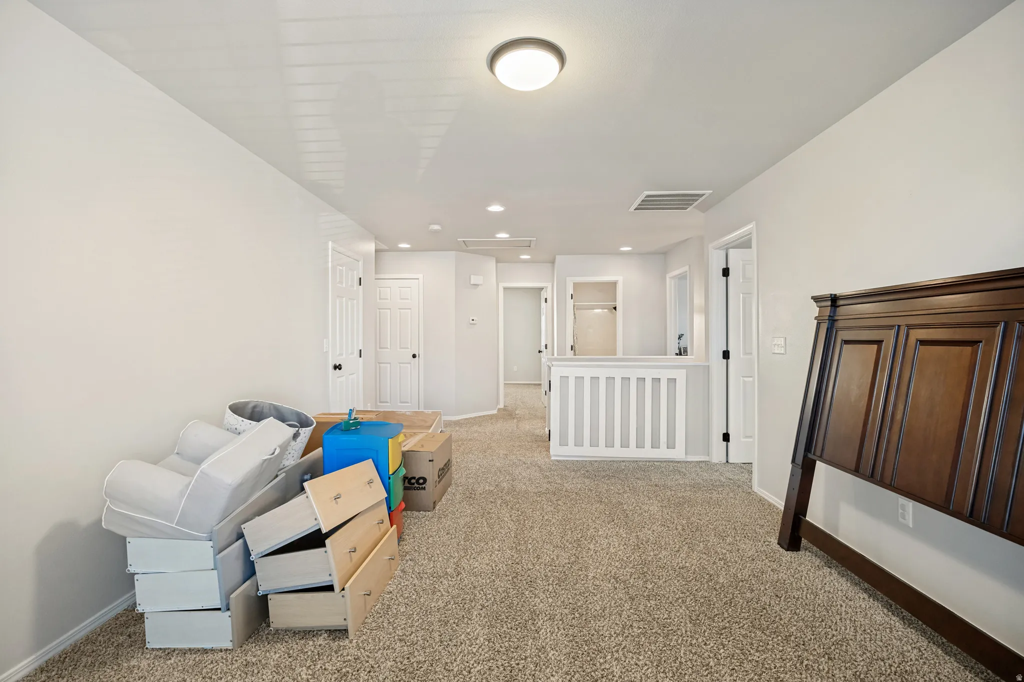 Open concept upper-level area with carpeted flooring, light neutral wall finishes, and a white balustrade overlooking a lower level