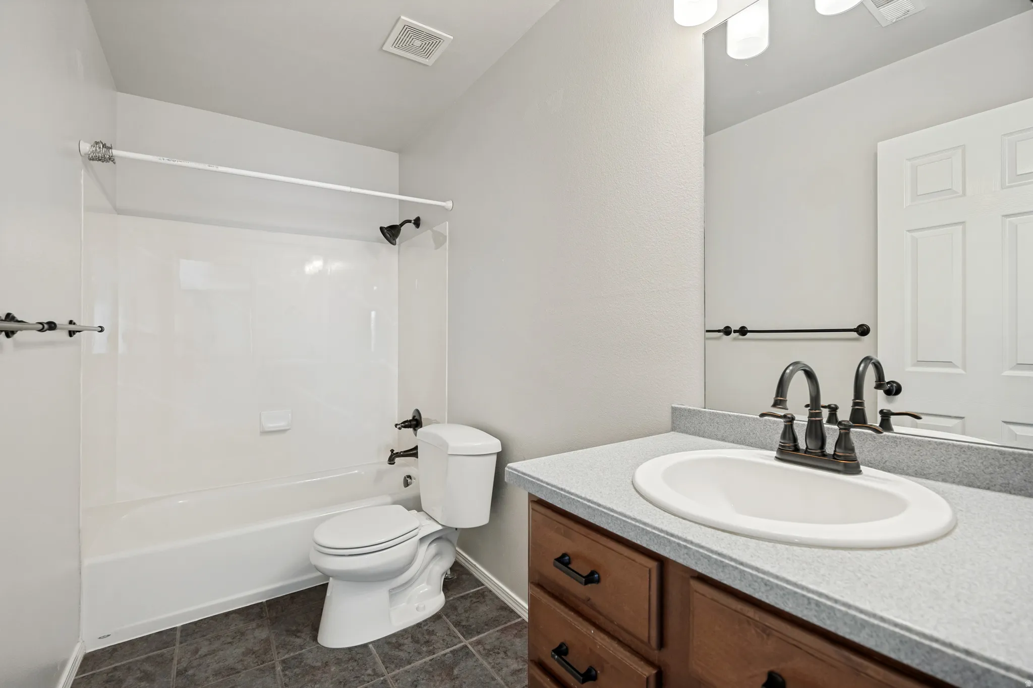 Full bathroom featuring a single vanity with a laminate countertop, dark wood-finish cabinetry, and a shower-over-tub combination with a white surround