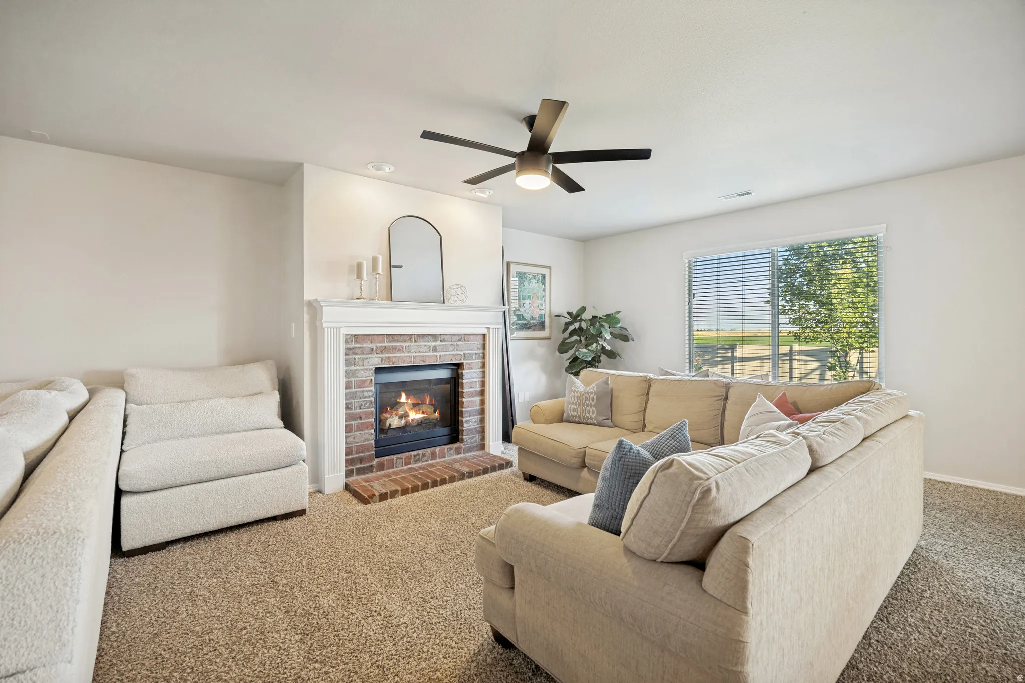 Living area featuring a brick fireplace with a white mantel, ceiling fan with integrated lighting, recessed lighting, and a large window