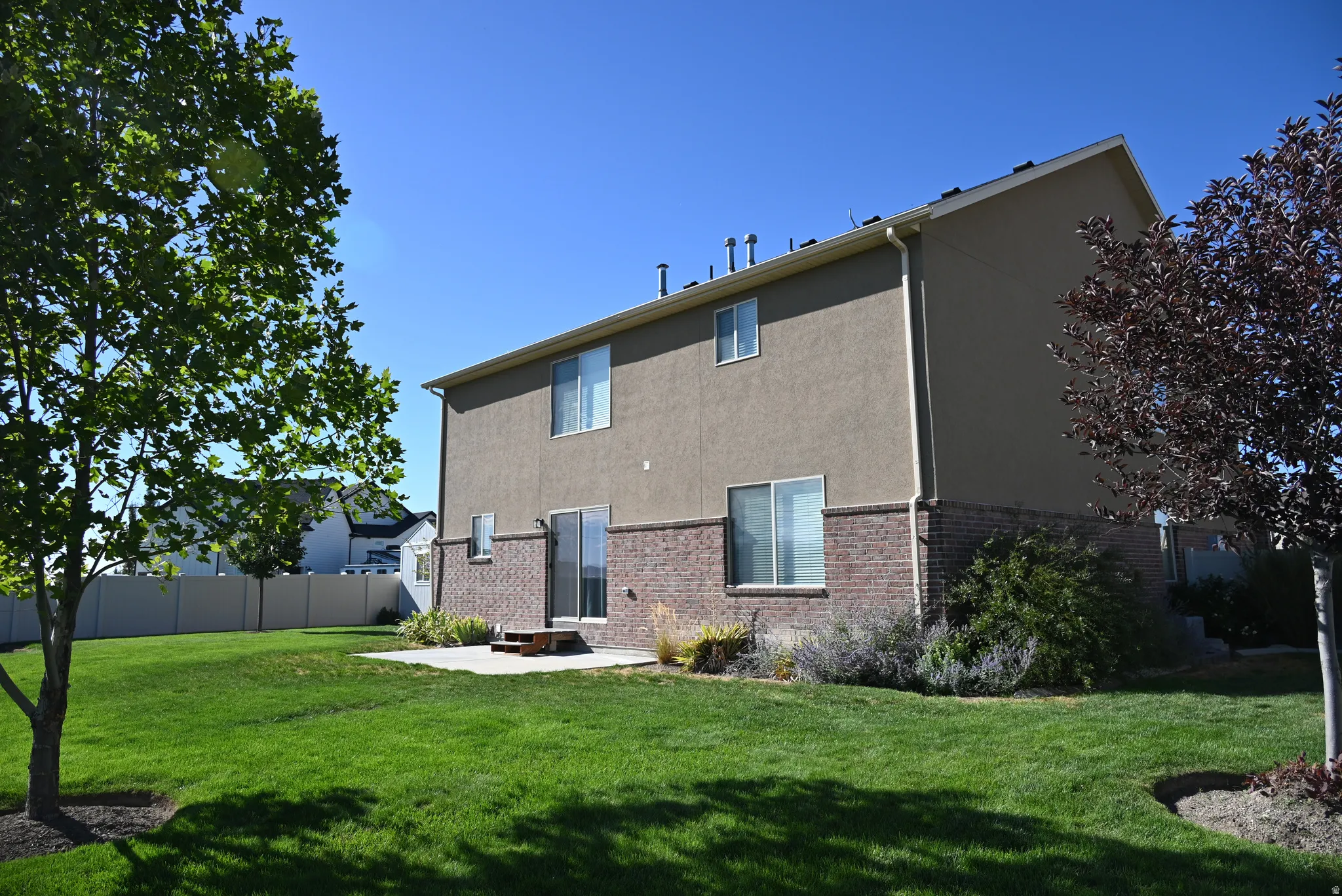 Expansive green lawn, stucco exterior, brick foundation, white vinyl windows, and a sliding glass door