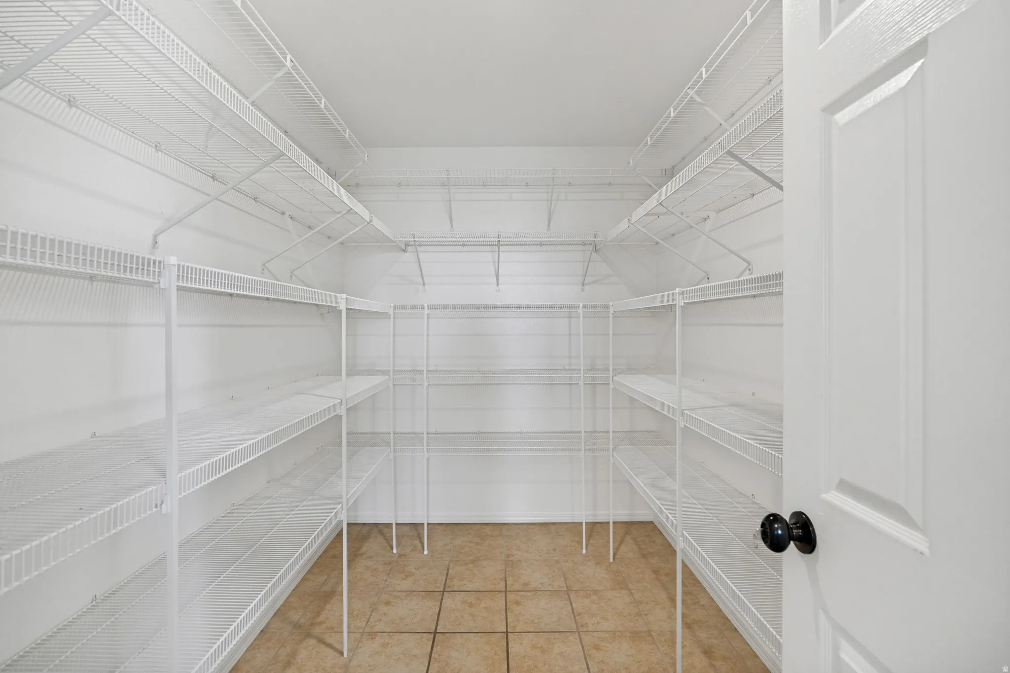 Spacious storage area featuring extensive white wire shelving, tiled flooring, and a panel door with black hardware