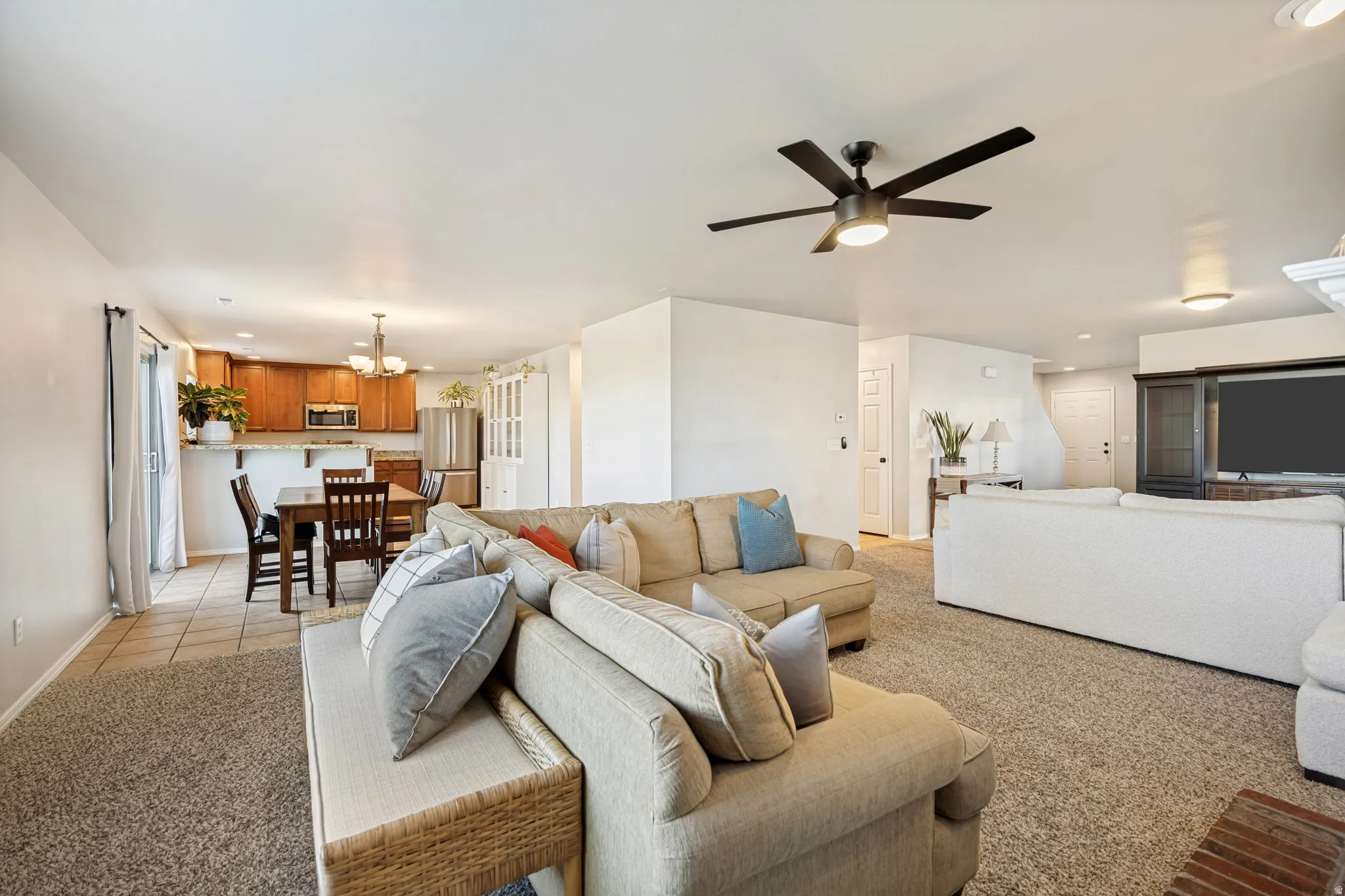 Expansive living space featuring a ceiling fan with light, plush carpet flooring, and white painted walls