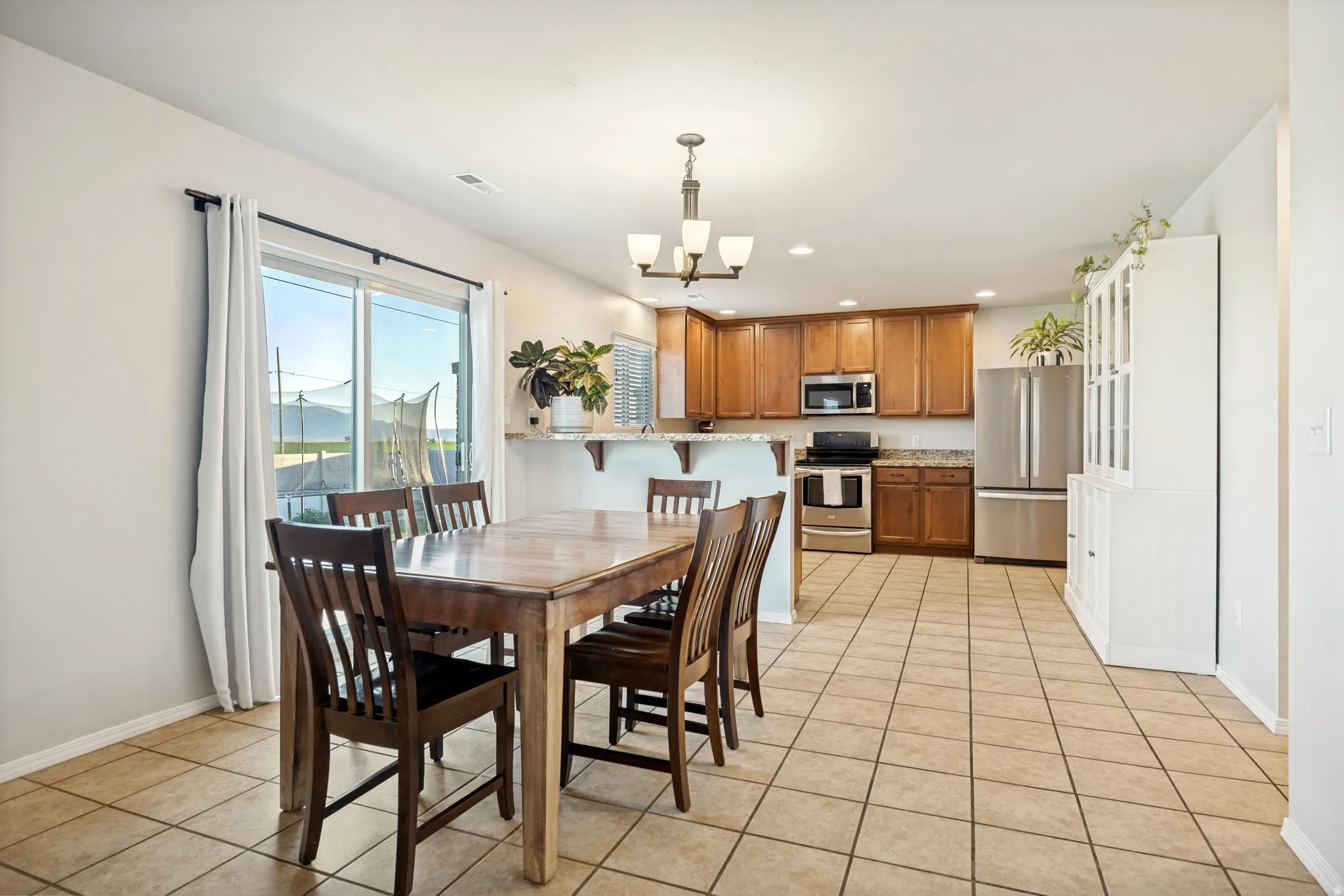 Open-concept kitchen and dining area featuring tile flooring, wooden cabinetry, stainless steel appliances, a breakfast bar, and a sliding glass door