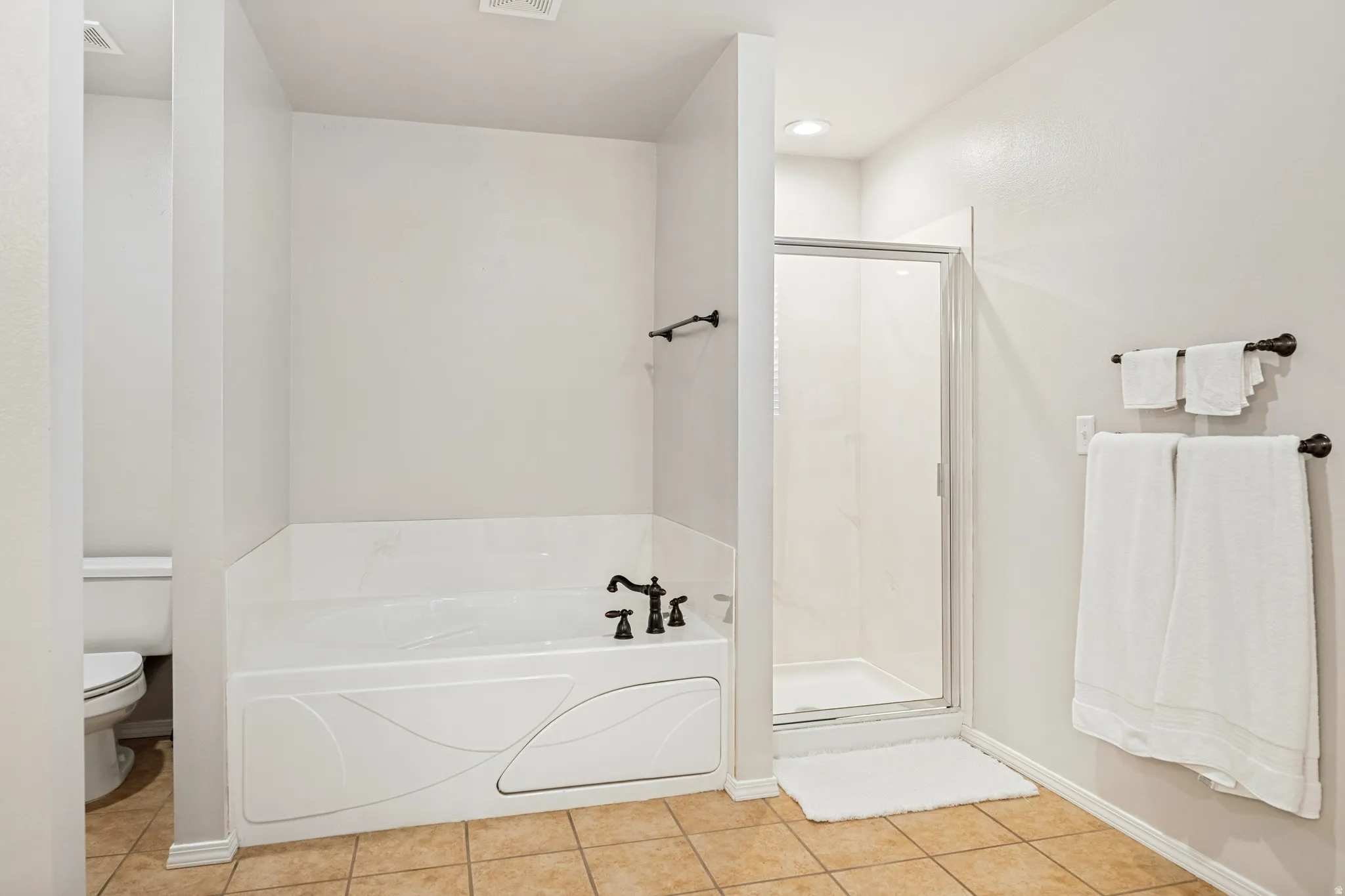 Bathroom featuring a built-in tub with dark bronze fixtures, an enclosed shower with a glass door, and square tile flooring