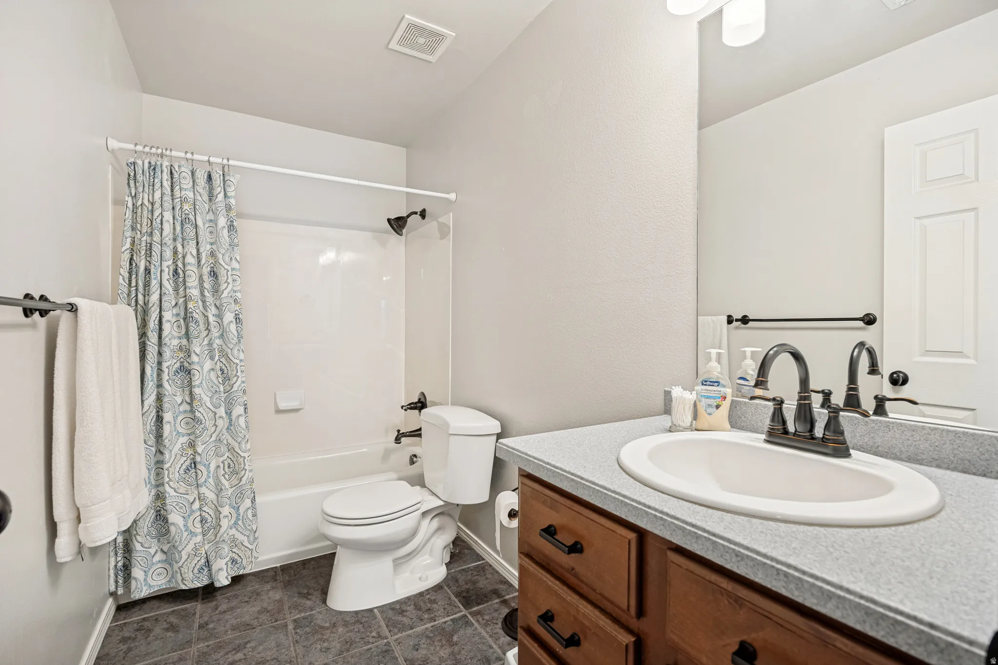 Bathroom featuring a white tub/shower combination, dark tile flooring, a single vanity with an oval sink, and a dark bronze faucet