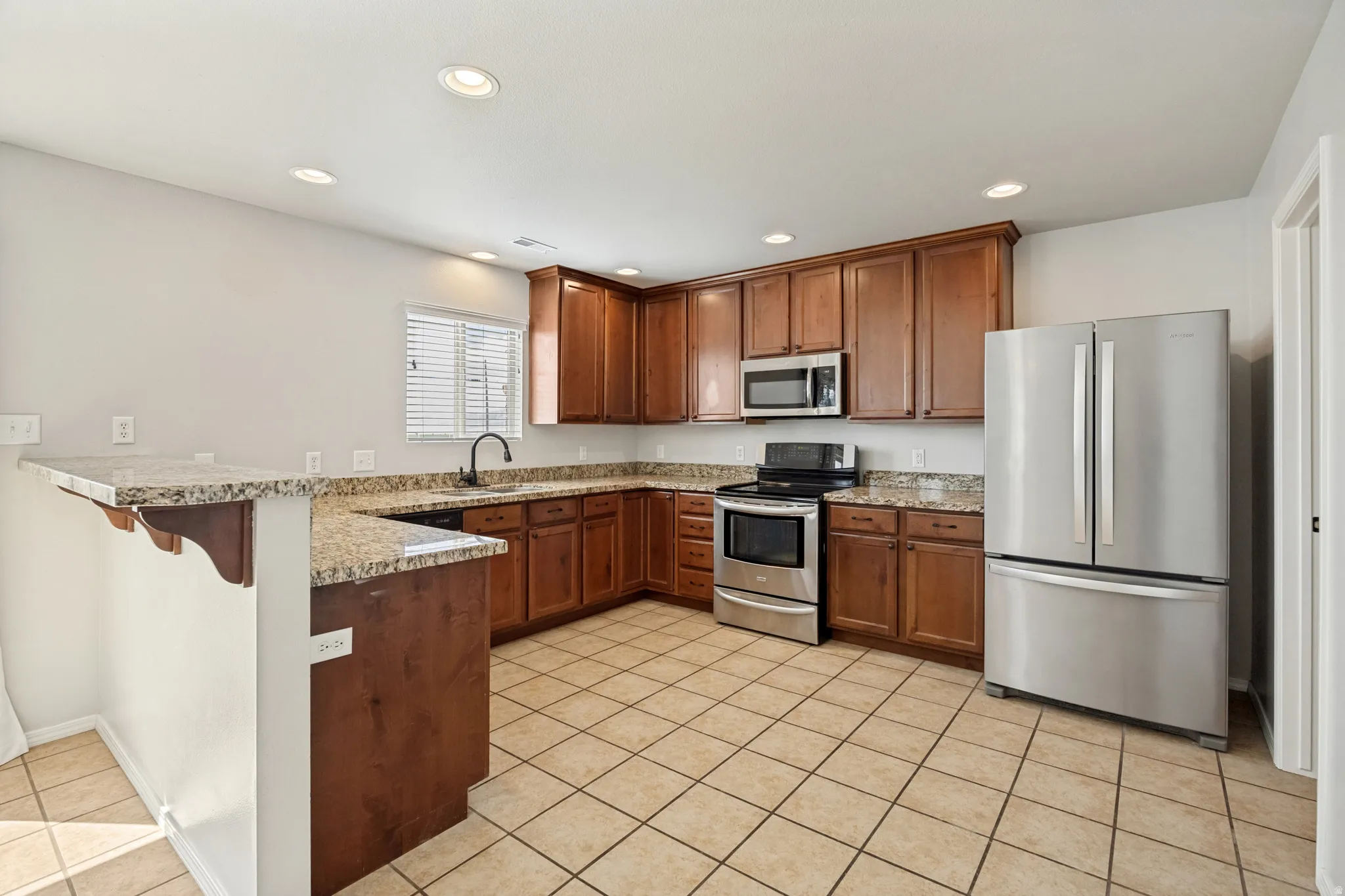 Kitchen featuring wood cabinetry, stainless steel appliances, granite-style countertops, tile flooring, and recessed lighting