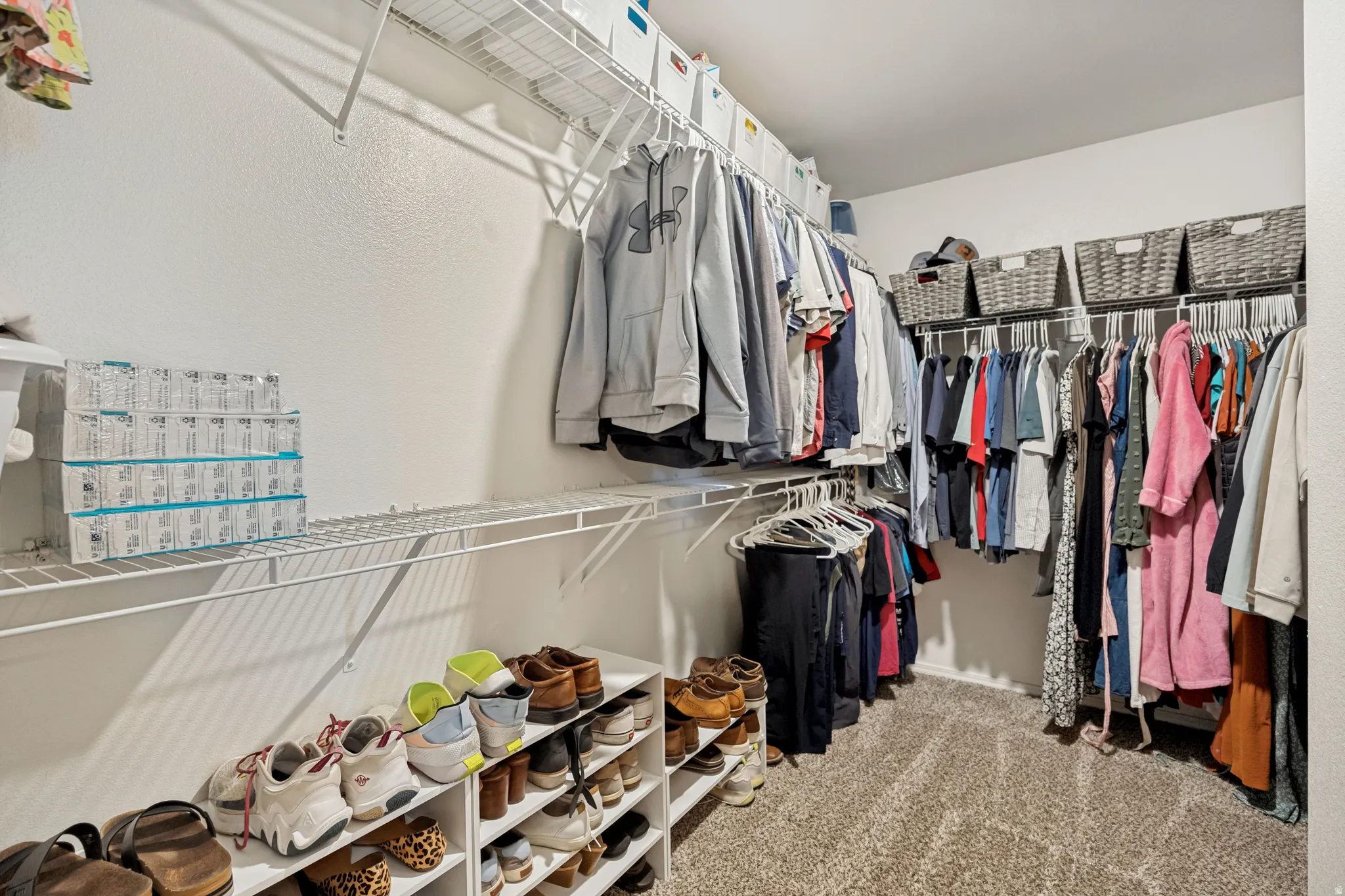 Spacious closet featuring white wire shelving, multiple hanging rods, and neutral carpet flooring