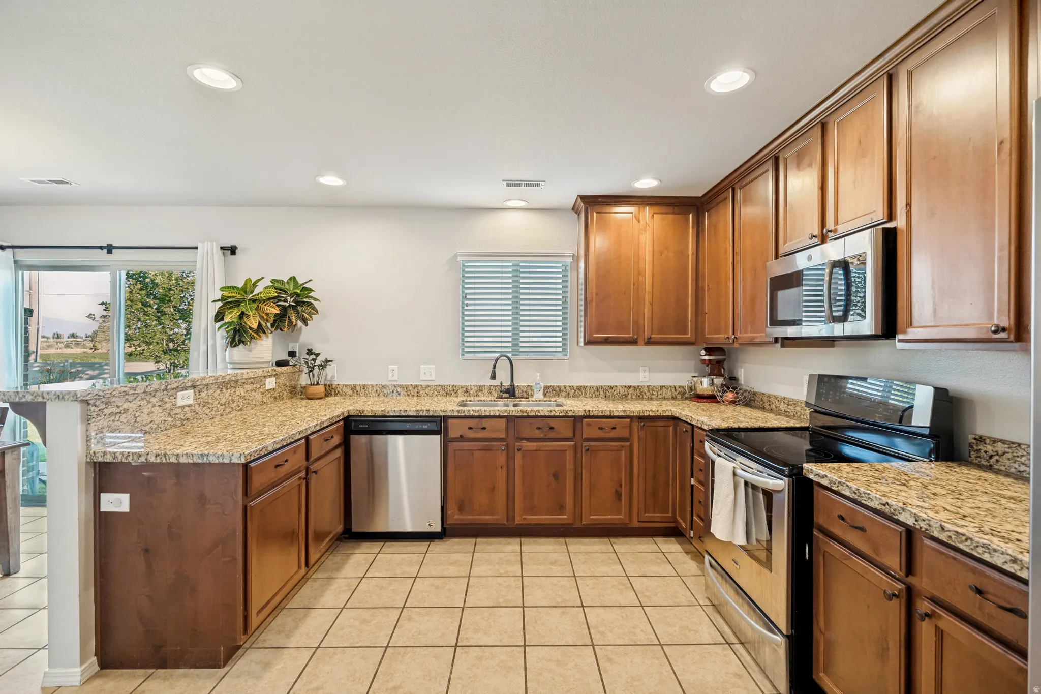 Kitchen featuring wood cabinetry, stainless steel appliances, granite countertops, tile flooring, and recessed lighting