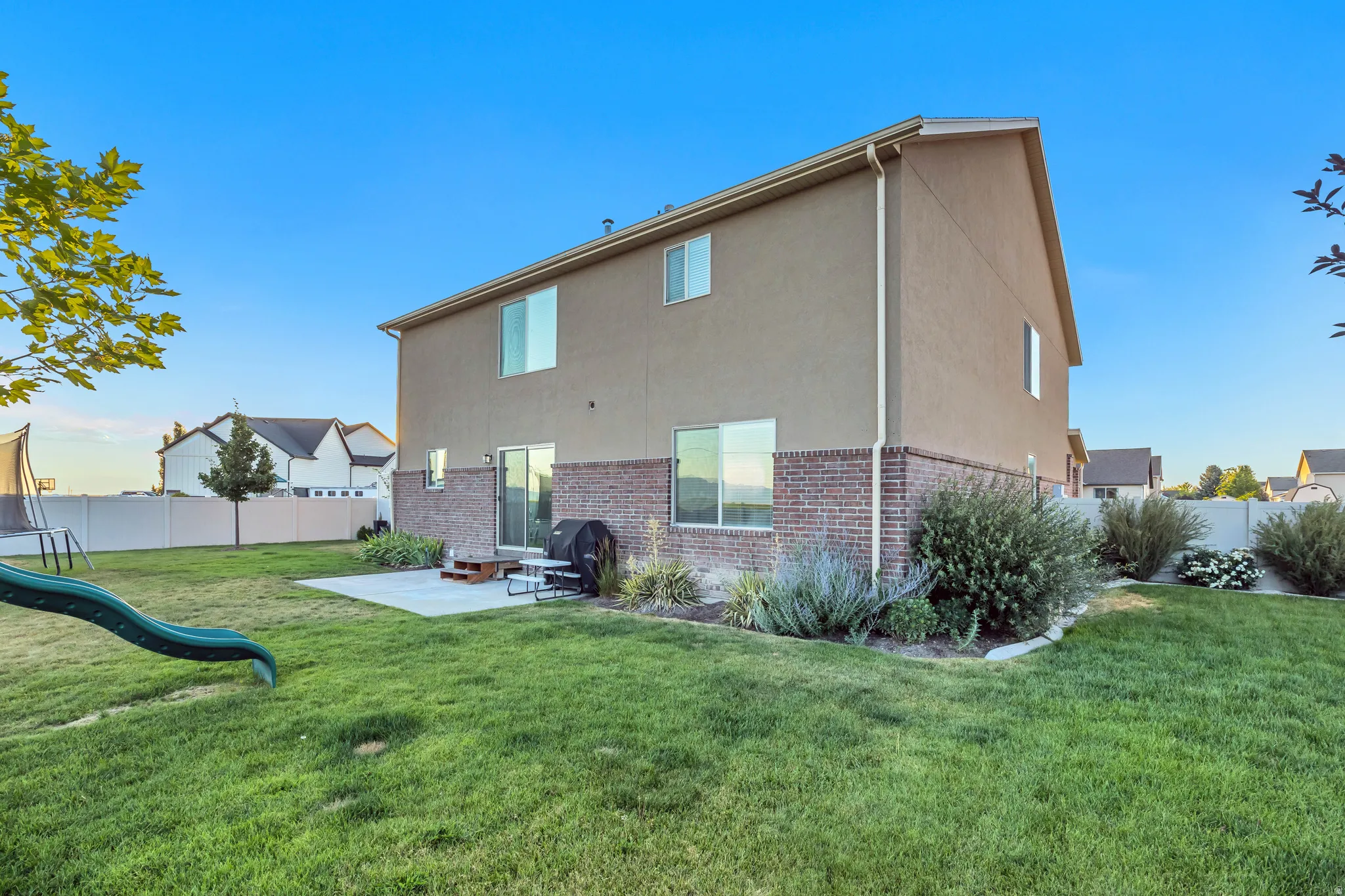 Expansive rear yard featuring a concrete patio, mature shrubs, and a well-maintained lawn