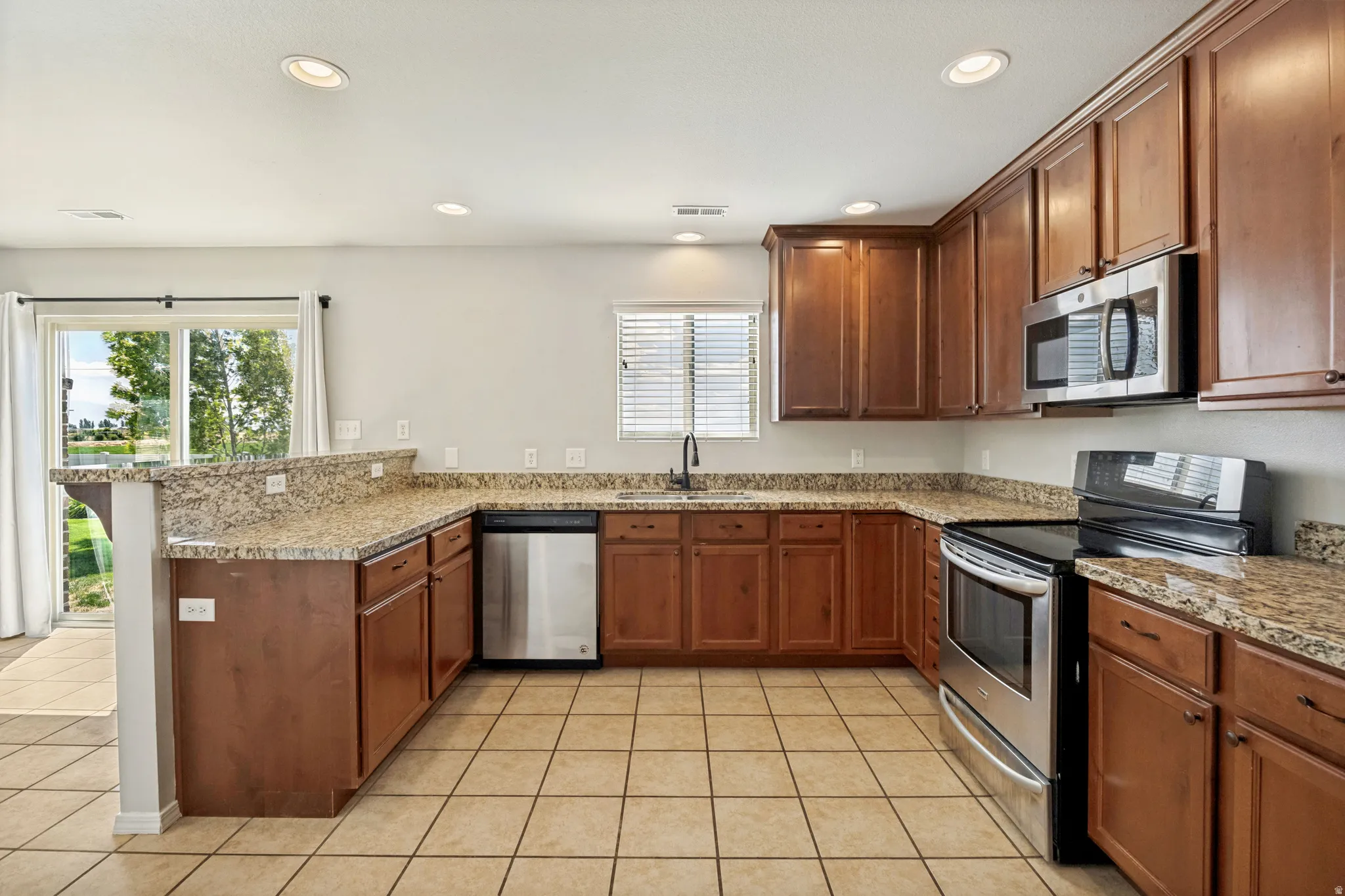 U-shaped kitchen featuring wood cabinetry, stainless steel appliances, granite-finish countertops, and tile flooring