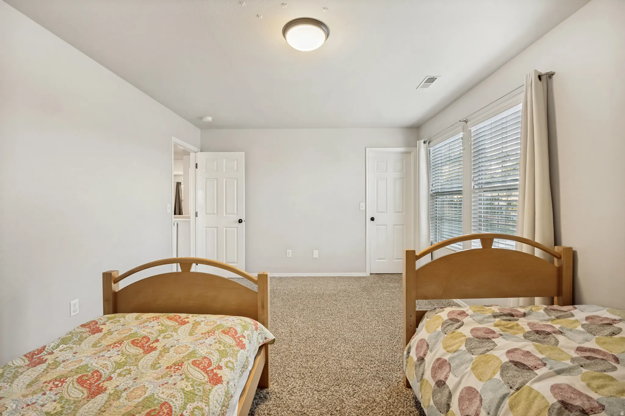 Carpeted room featuring light gray walls, two paneled doors with black hardware, and a window with blinds and curtains
