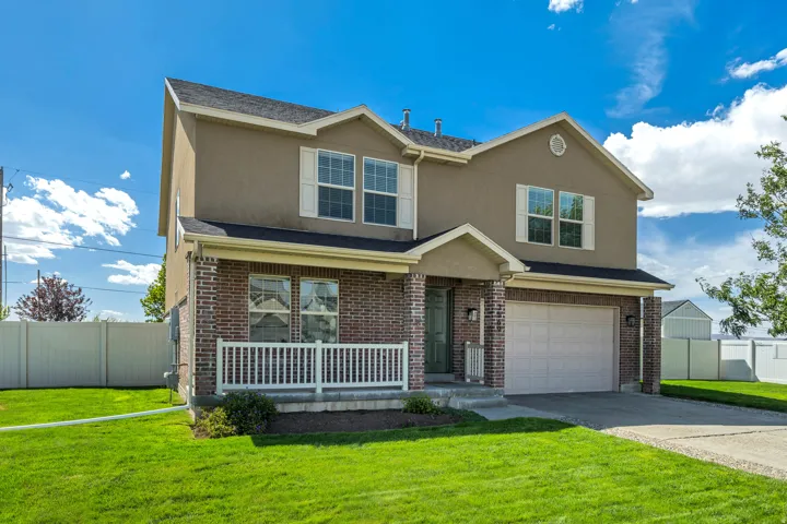Two-story residence featuring a brick facade, stucco siding, an attached garage, a covered front porch with white railing, and a vibrant green lawn