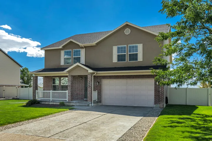 Two-story residence featuring a brick and stucco exterior, covered front porch with white railing, attached two-car garage, and established landscaping