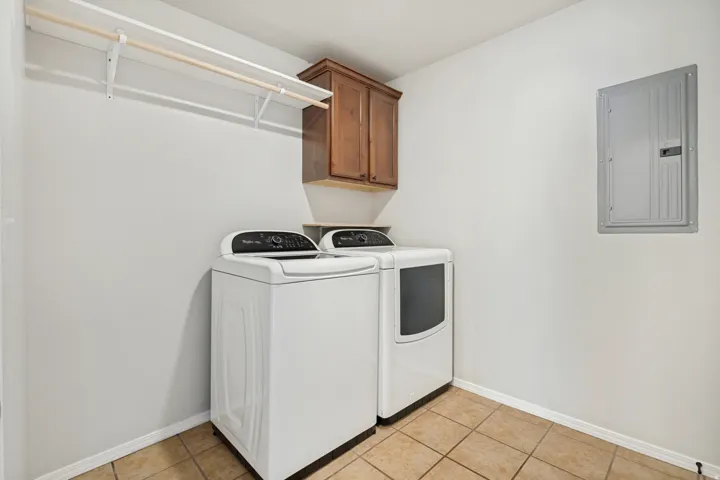 Laundry area featuring a wood-finish storage cabinet, wall-mounted clothes rack, and tiled flooring