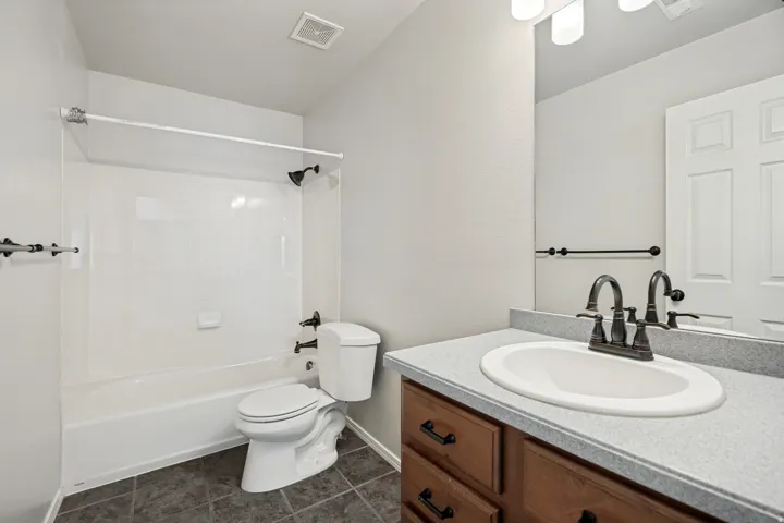 Full bathroom featuring a single vanity with a laminate countertop, dark wood-finish cabinetry, and a shower-over-tub combination with a white surround
