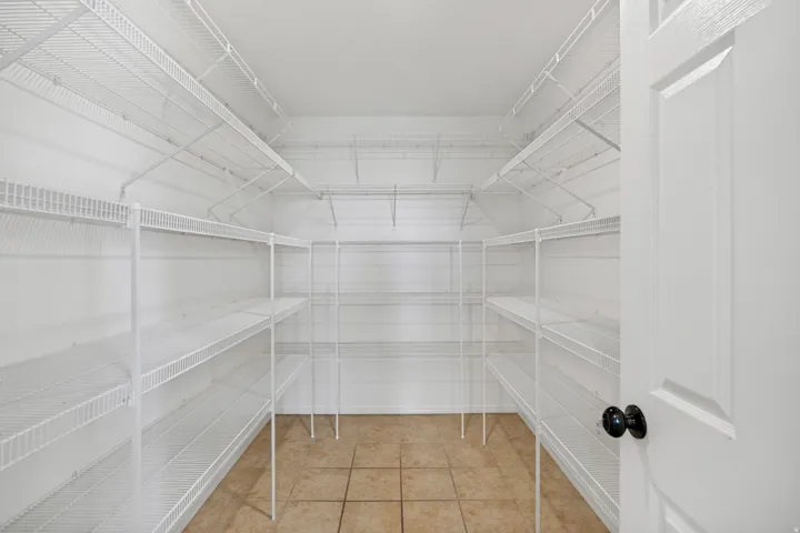 Spacious storage area featuring extensive white wire shelving, tiled flooring, and a panel door with black hardware