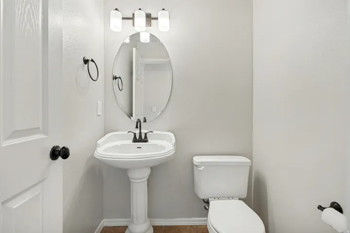 Pedestal sink with dark-toned fixtures, oval mirror, and a three-light vanity fixture
