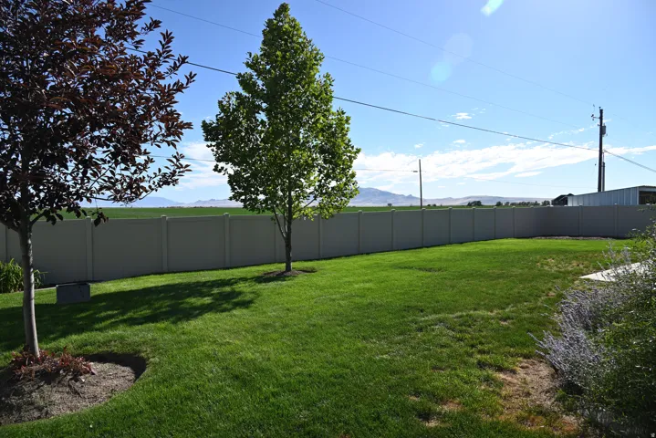 Manicured lawn with a privacy fence, established trees, and a distant mountain range