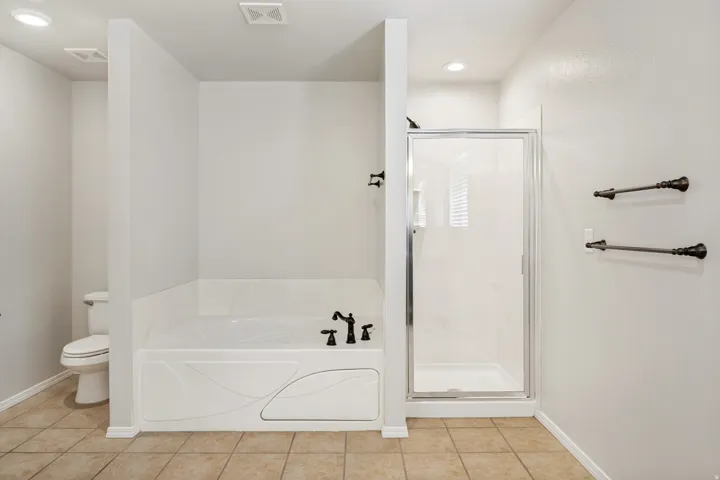 Tiled flooring, white soaking tub with dark fixtures, and a glass-enclosed shower