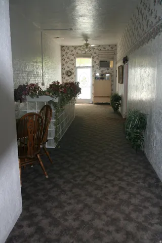 Hallway featuring patterned carpet flooring, textured wallpaper, a ceiling fan, and a glass block partition