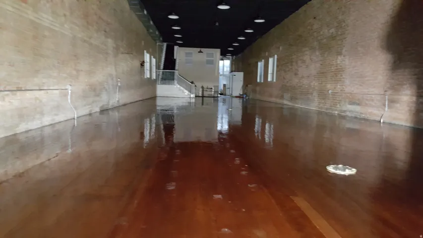 Expansive interior space featuring a high-gloss wood-finish floor, exposed brick walls, and a black ceiling with recessed lighting