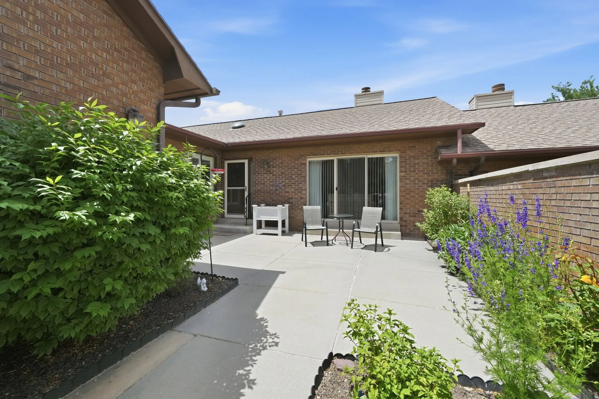 Private patio area with concrete surfacing, brick exterior, and mature landscaping