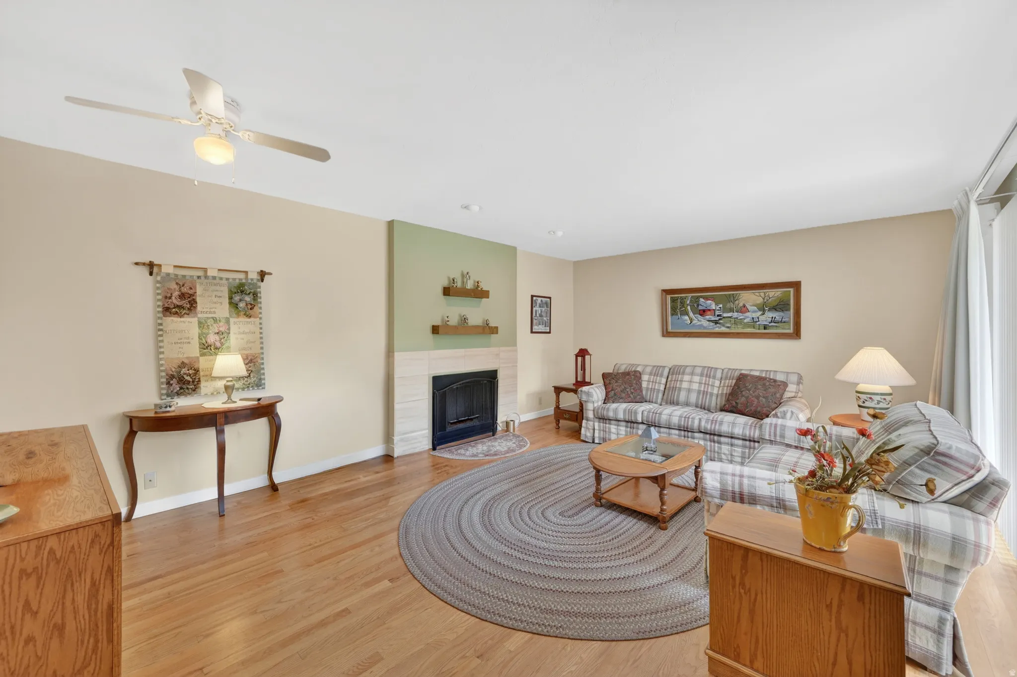 Living room featuring natural oak wood flooring, a fireplace with a light-toned surround, a ceiling fan with integrated lighting, and a slider door