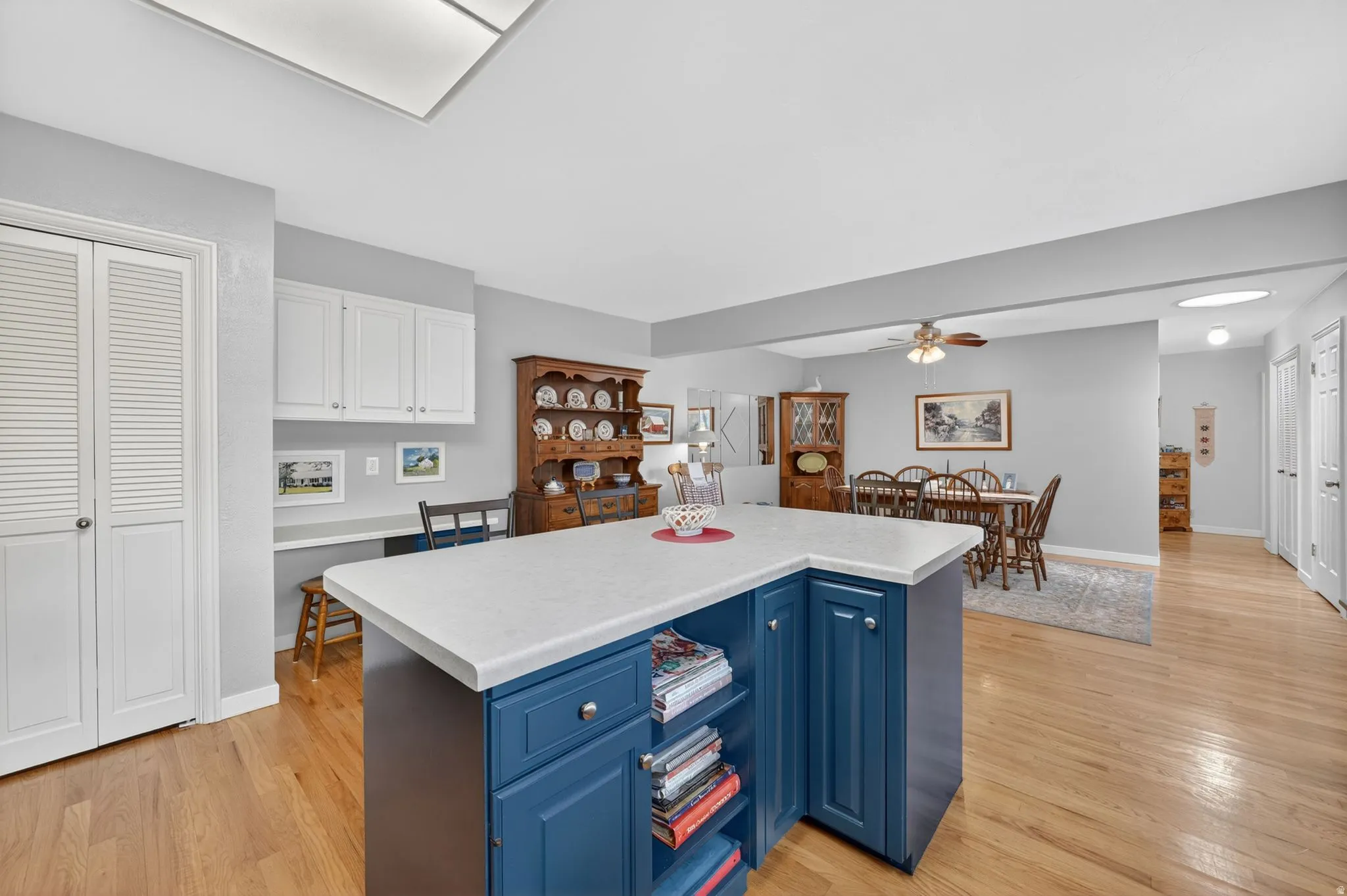 Kitchen featuring a blue island with a solid surface countertop, wood-finish flooring, and a built-in desk area with white upper cabinetry