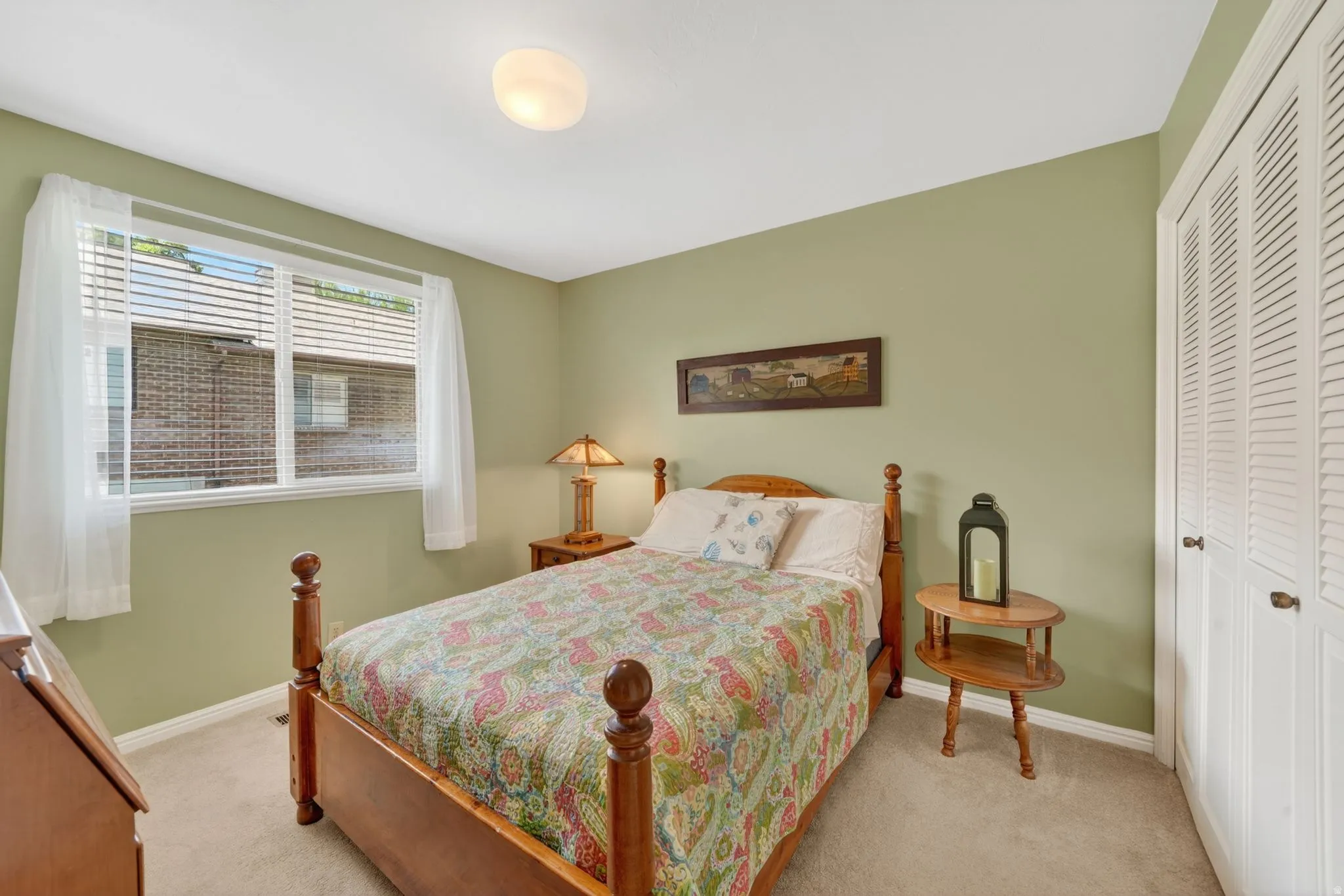 Bedroom featuring carpet flooring, a large window with blinds and sheer curtains, a flush-mount ceiling light, and white louvered bifold closet doors