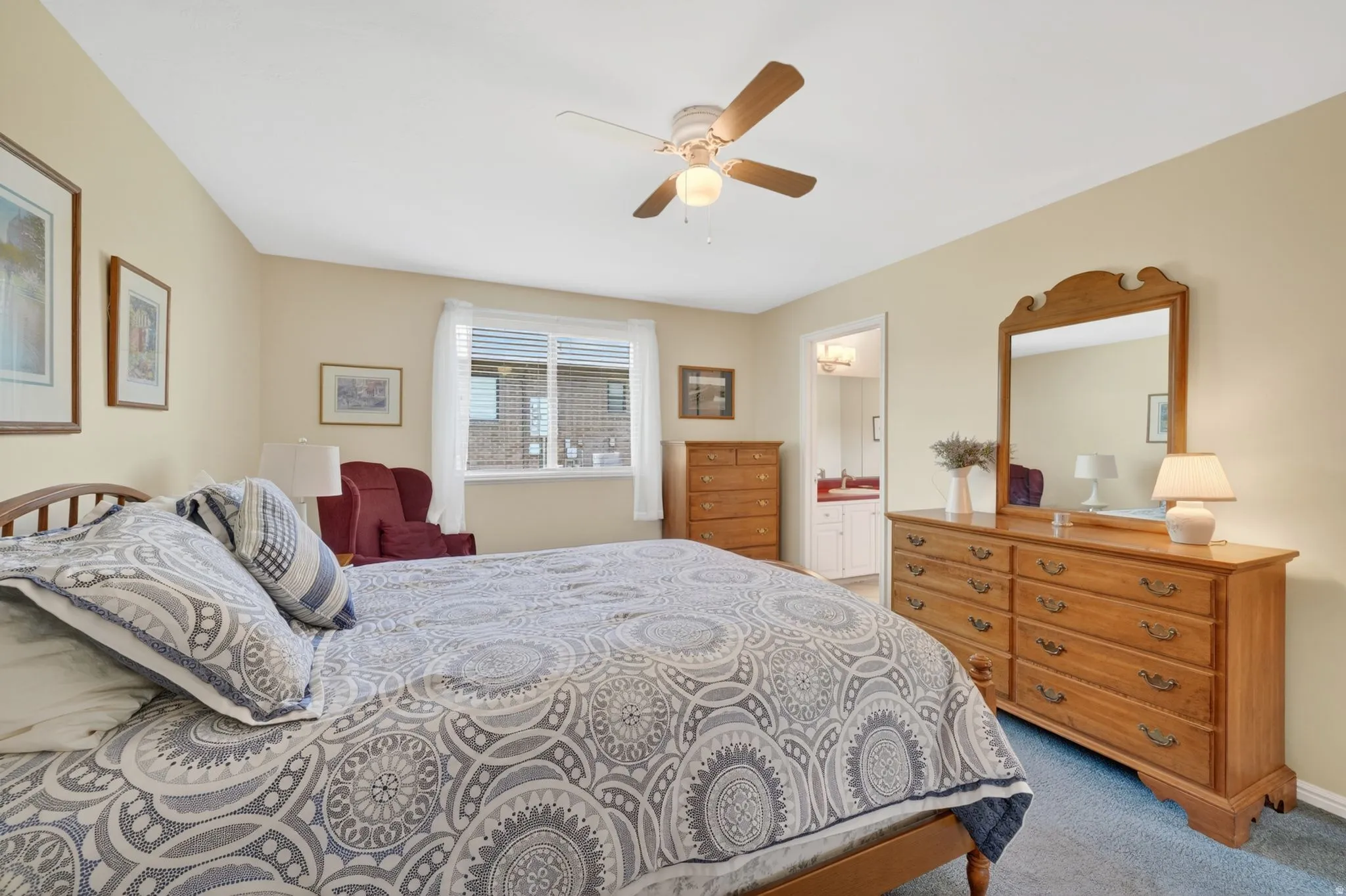 Carpeted bedroom featuring a ceiling fan with integrated lighting, a window with blinds and drapes, and an open doorway leading to an additional space