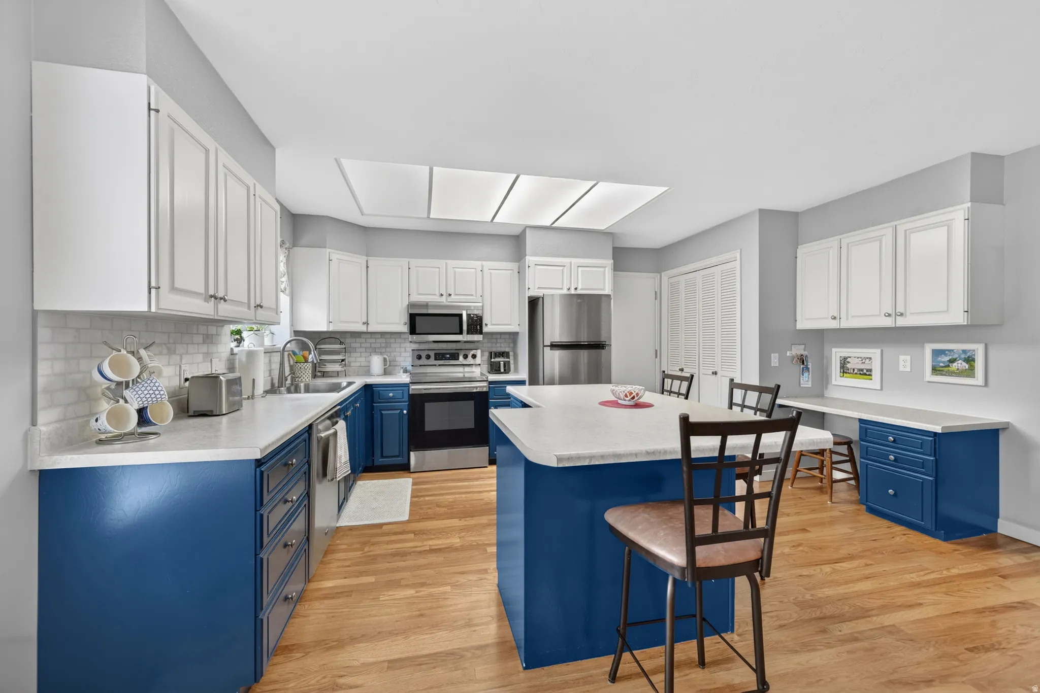 Spacious recently updated kitchen featuring an expansive center island, white countertops, natural oak wood flooring, white upper cabinetry, and blue lower cabinetry