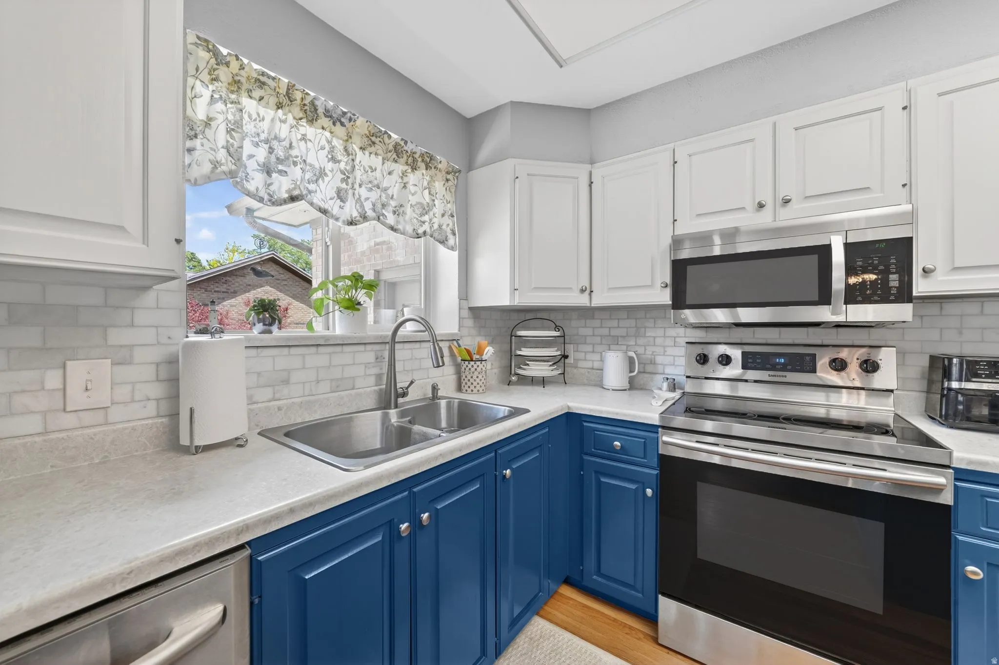 Kitchen featuring white upper cabinetry, blue lower cabinetry, stainless steel appliances, a double basin sink, and a tiled backsplash