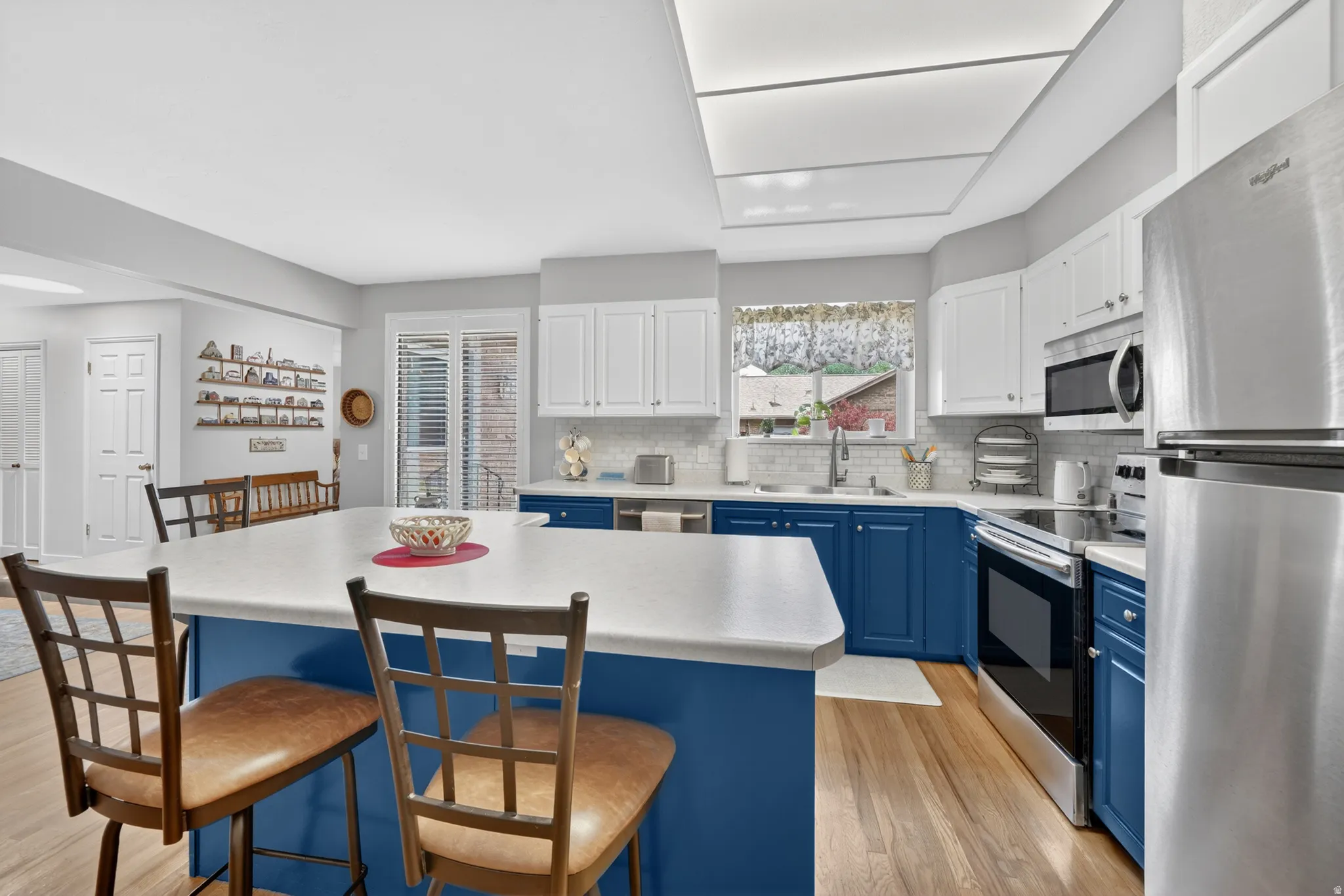 Kitchen featuring a central island with countertop seating, two-tone cabinetry, stainless steel appliances, and natural oak wood flooring