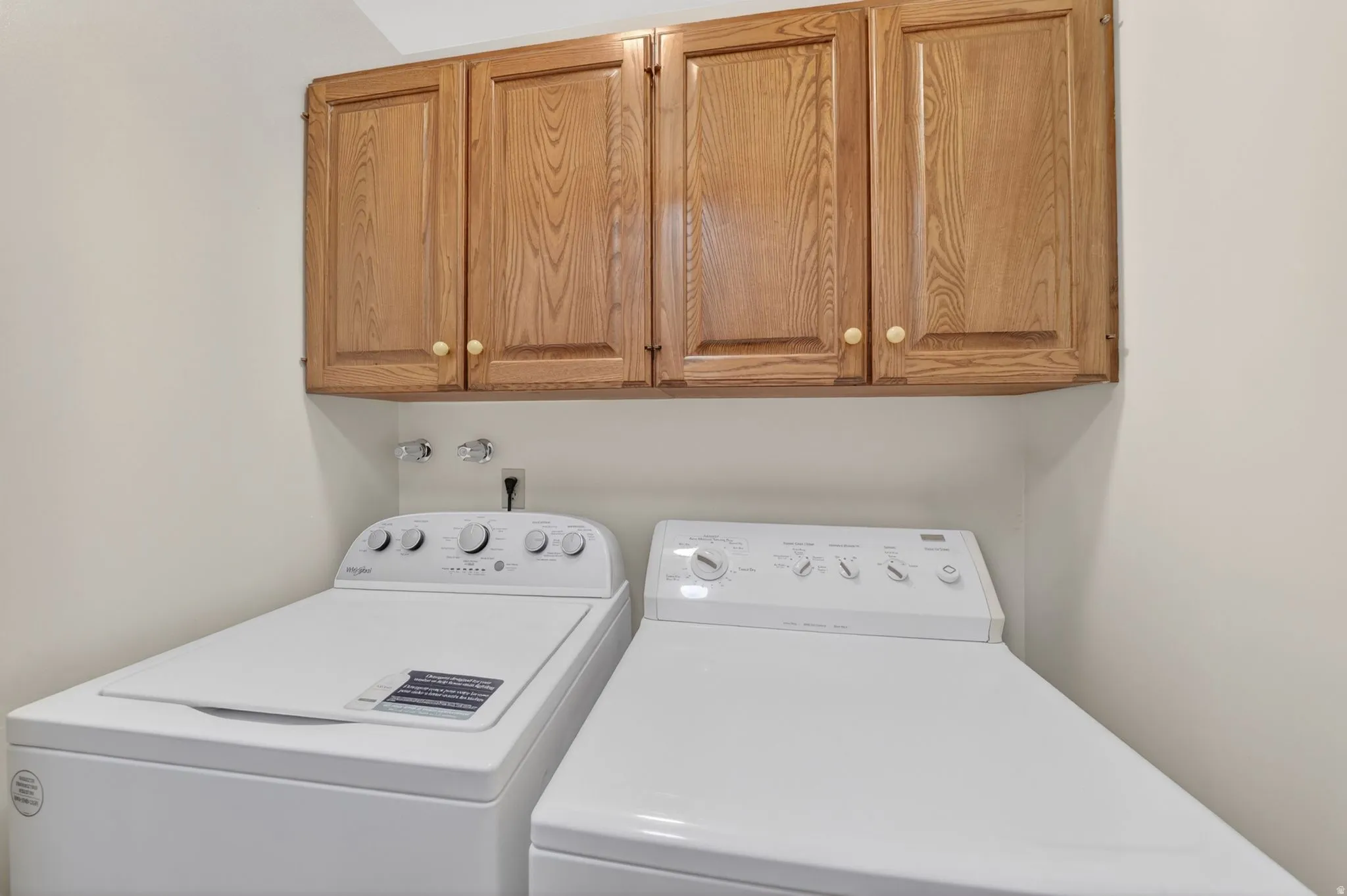 Laundry area featuring upper wood cabinetry with knob hardware and white appliances
