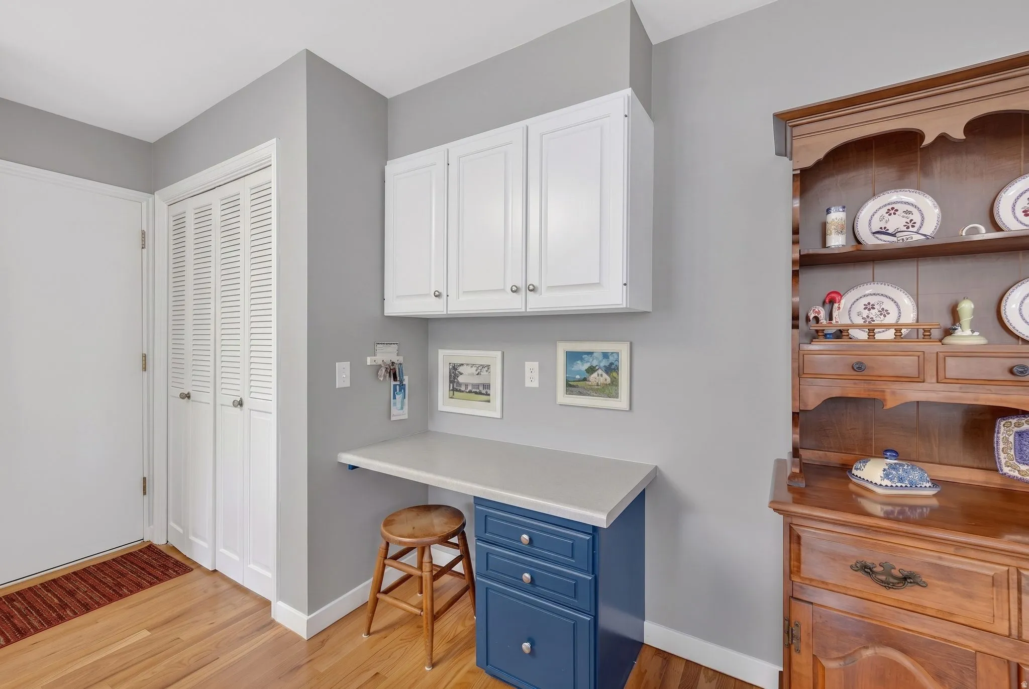 Built-in desk area featuring white upper cabinetry, a light-toned countertop, and blue lower drawers