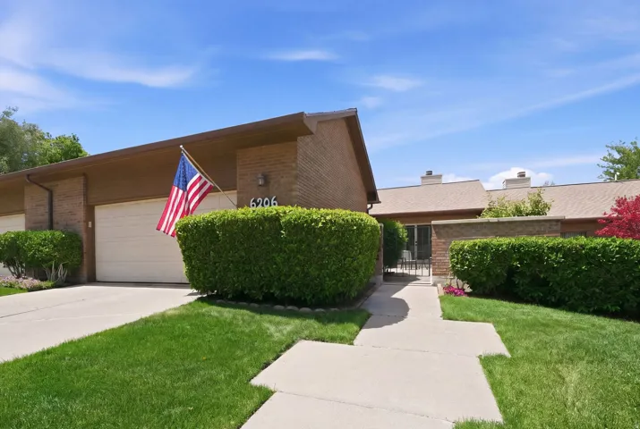 Brick exterior with an attached garage, a paved driveway, and manicured green lawns