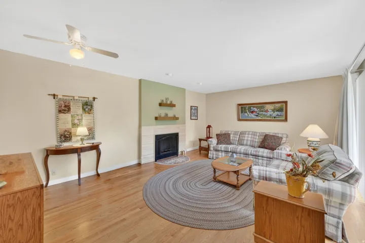 Main level Living room featuring natural oak wood flooring, a fireplace with surround, ceiling fan, and a slider door leading to patio area