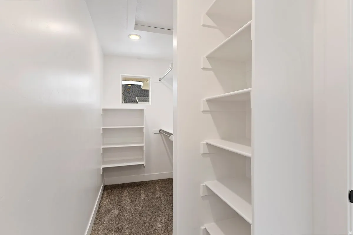 Spacious walk-in closet featuring white built-in shelving, hanging rods, recessed lighting, and a window for natural light