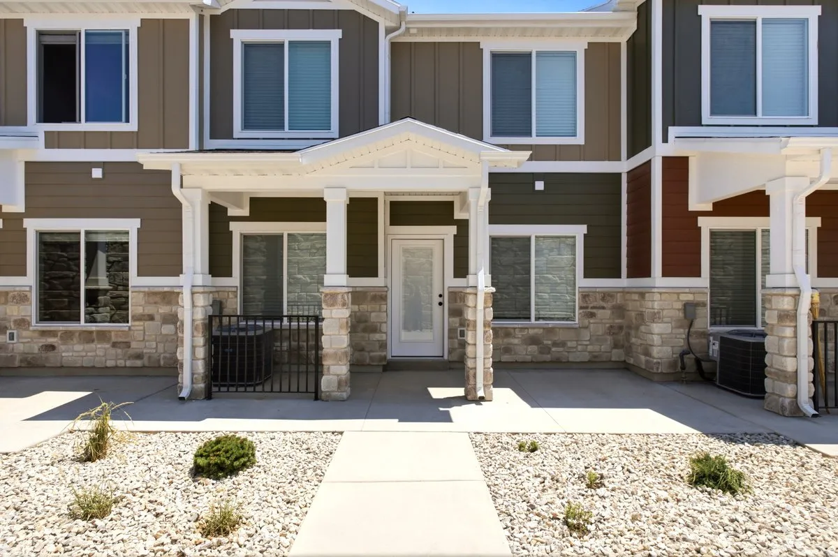 Multi-story residence featuring a covered entry, stone veneer accents, and a panel-style entry door with frosted glass