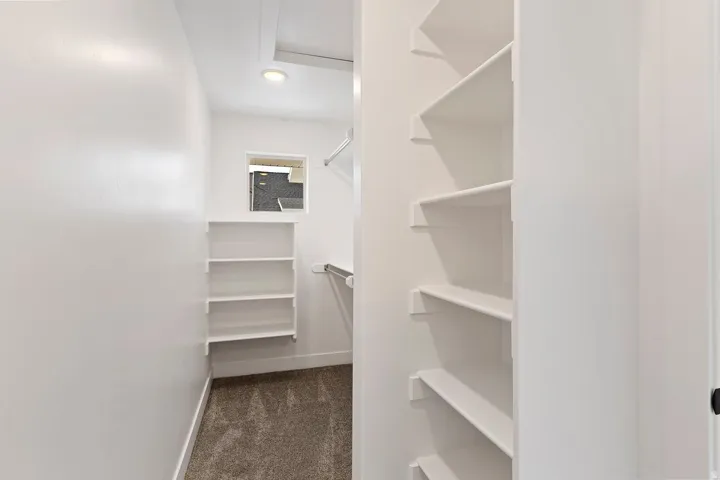 Spacious walk-in closet featuring white built-in shelving, hanging rods, recessed lighting, and a window for natural light