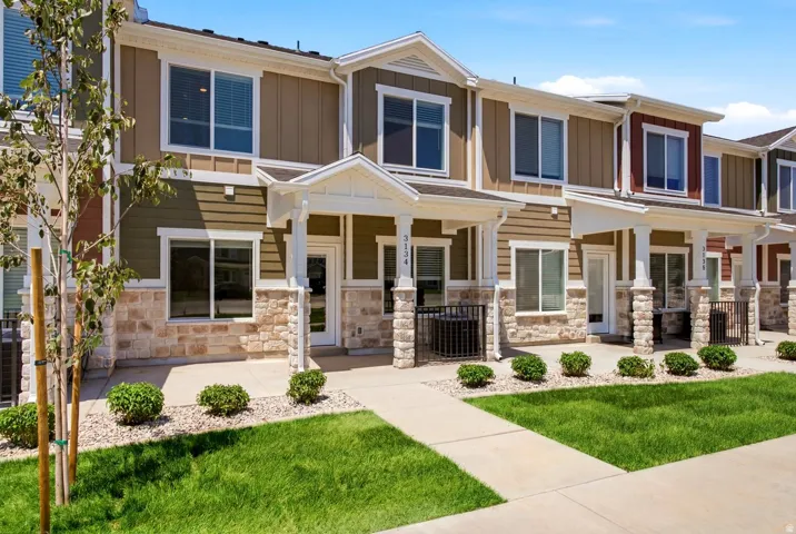 Modern townhome exterior featuring multi-toned siding, stone accents, white trim, a covered entry, and a manicured lawn