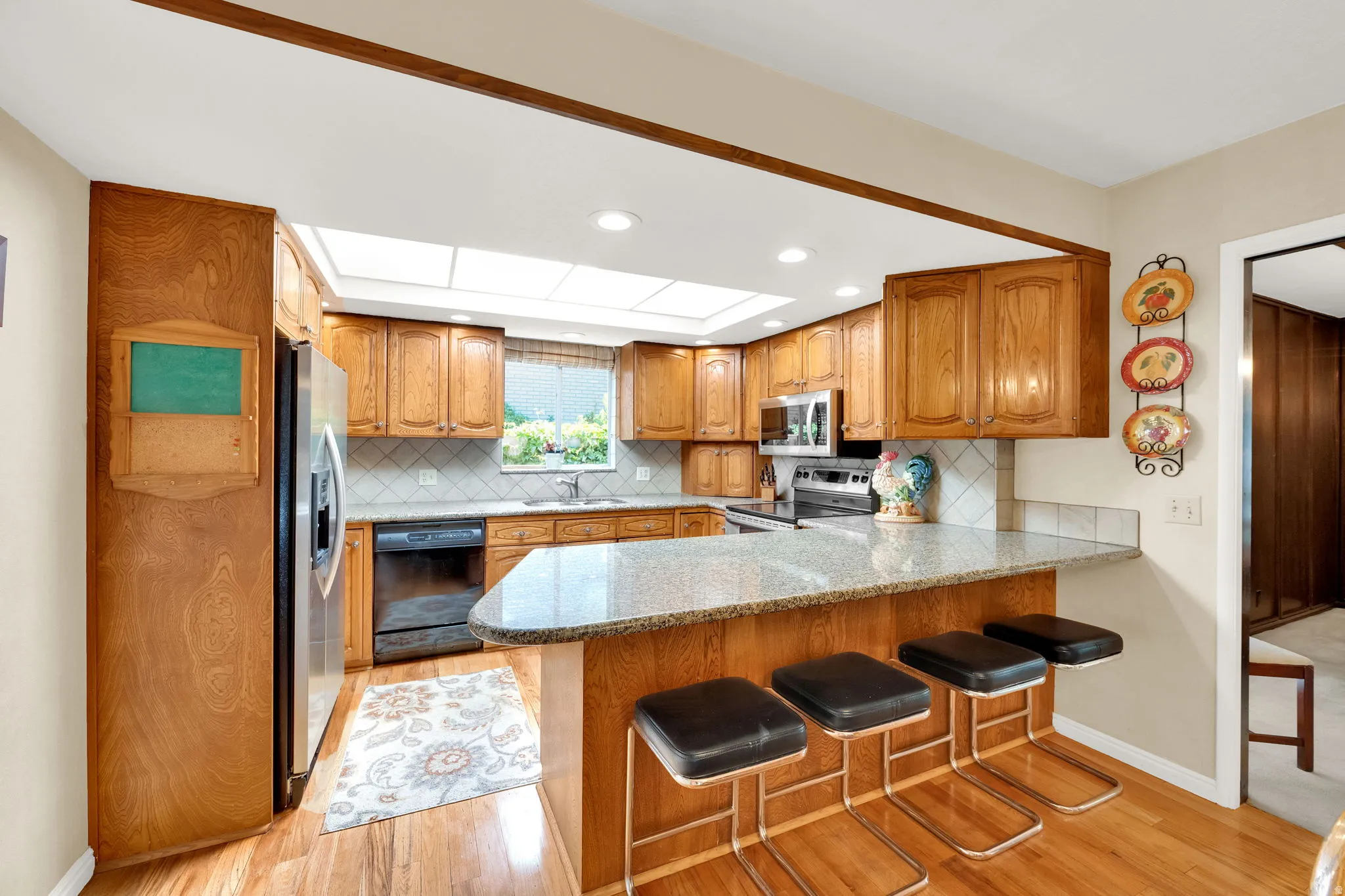 Kitchen featuring wood cabinetry, a granite-finish countertop, stainless steel appliances, a tile backsplash, and wood-finish flooring