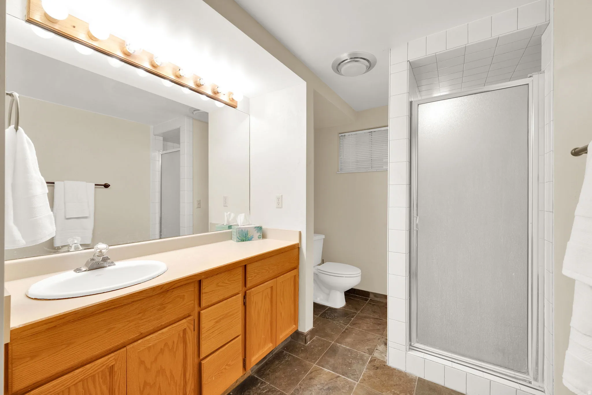 Bathroom featuring a light wood-finish vanity with an integrated sink, a large mirror, and a multi-bulb light fixture